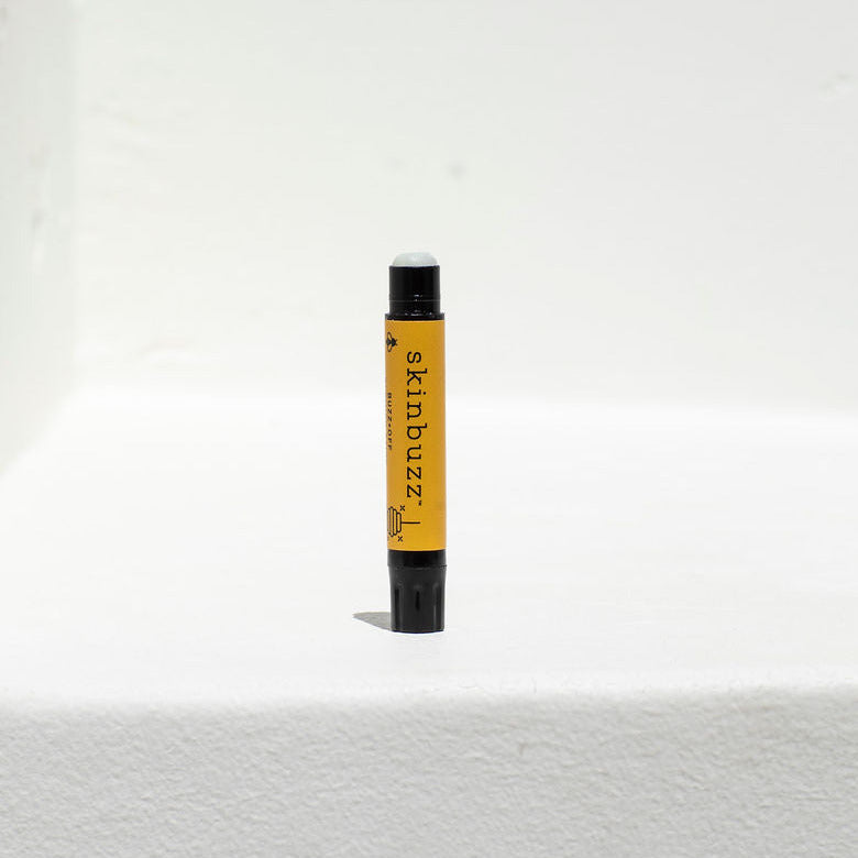 
                  
                    A single blemish stick tube standing upright on a white textured surface against a white wall. The tube is black with a bright yellow label that reads 'skinbalm' vertically in black text.
                  
                